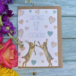 Eco card from JW Art depicting boxing hares with a colourful floral twist with the words Greetings from the Cotswolds.