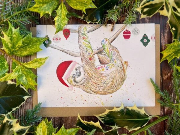 Sloth eco friendly Christmas card. Sloth hanging with baubles and a Santa hat